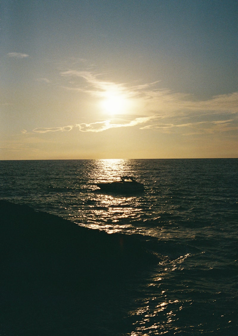 The sun is setting over the ocean with a boat in the water