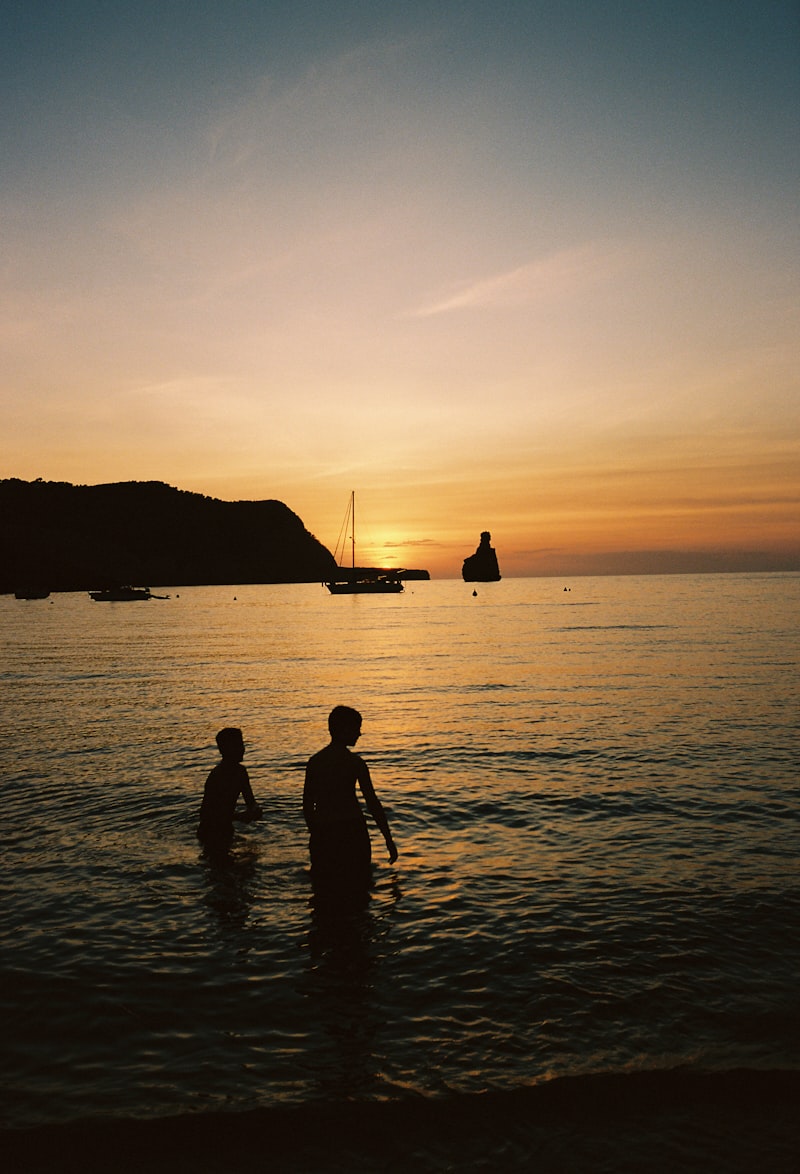 Two figures wading in the ocean at sunset.